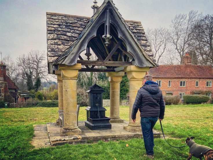 Jim and Jett whippet looking at the pump on Ockley village green called Scott's Well